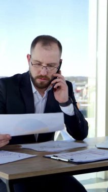 İş yerinde çalışan bir iş adamı. Gözlüklü, masada dizüstü bilgisayarıyla oturan ve ofisteki evraklara bakan kendine güvenen bir adam. Dikey video