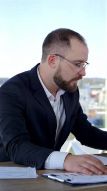 Ofisteki sinirli iş adamı. Ofis çalışanı masasında otururken bazı zorluklar karşısında morali bozuldu. Takım elbiseli kızgın adam iş yerinde kağıtları dağıtıyor. Dikey video