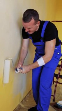 Yeni tarz yenileme. Üniformalı işçiler duvarları boya rulosuyla boyarlar. Duvarları boyayan bir patenci. Dikey video