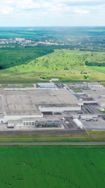 Tarlalar arasında sanayi kompleksi. Yeşil doğal ortamda büyük bir üretimin panoramik görüntüsü. Hava görüntüsü. Geri çekilin. Dikey video