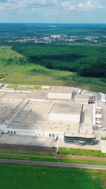 Güneş ışığında büyük bir sanayi fabrikasının çatıları. Çağdaş beyaz bina fabrikası. Yeşil arazide araba ve kamyonlar için yerler var. Dikey video