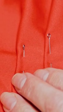 Kalıpları yakın planda tutmak. Dikey video atölyesinde kadın terzinin kumaş dikme görüntüsünü kapat