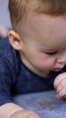 Sevimli küçük oğlan karnının üstüne yatar ve yanında bir emzik taşır. Tatlı çocuk başını kaldırıp tatlı tatlı gülümsemeye başlıyor. Kapatın. Arkaplan bulanık. Dikey video