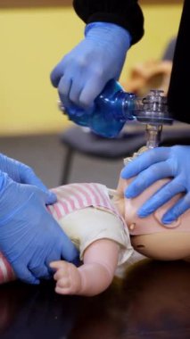 Öğrenciler bebek üzerinde kalp masajı yapıyor. Bir mankenin üzerinde insanların hayatını kurtarmak için gereken tıbbi prosedürü öğreten eğitmen. Dikey video