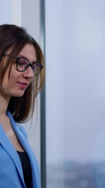 Mavi ceketli esmer kadın bilgisayarda çalışıyor. Kadın dizüstü bilgisayarda, yumuşak bir sandalyede oturuyor. Düşük açı görünümü.