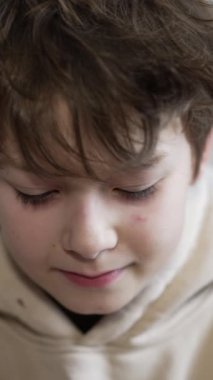 Koyu renk saçlı genç çocuk aşağı bakıyor ve doğruca kameraya bakıyor. Kapatın. Gülümseyen bir çocuğun portresi. Işık arkaplanı.