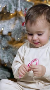 Beyaz tişörtlü beyaz çocuk elinde baston şeker tutuyor. Çocuk şekeri kırıyor ve yere atıyor..