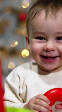 Küçük oğlan hapşırır ve mutlu bir şekilde güler. Çocuk ellerini sallayarak oyuncak piramitle oynuyor. Kapatın. Arkaplanda bulanık bir Noel ağacı.
