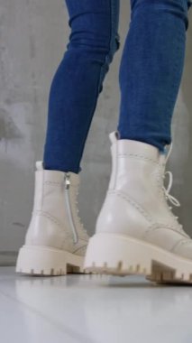 Kot giyen bir kadının üzerinde beyaz deri asker botları. Stüdyoda şık ayakkabılar sergileyen kadın..