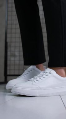 Süslü, kar beyazı spor ayakkabıları ve bir mankenin bağcıkları. Siyah pantolon giyen ve stüdyoda poz veren bir adam. Kapat..