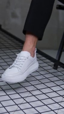 Modern kullanışlı beyaz spor ayakkabılar. Erkek model sandalyede oturur ve ayaklarını kameraya yakın bir yerde tutar..