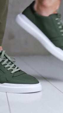 Erkek, rahat ve şık spor ayakkabılar giymenin göstergesi. Adam haki rengi ayakkabılarıyla stüdyonun beyaz zemininde zıplıyor. Kapat..