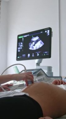 Hamile kadın ve kocası doktorun kabinesindeler. Kadın doktor, sensörü koca bir kadının karnıyla hareket ettiriyor..