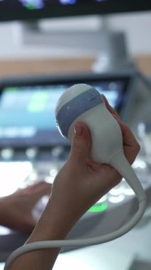 Doğum uzmanı sensörü tutuyor ve ultrason makinesinin tuşlarına basıyor. Doktor hamile bir kadının muayenesini başlatıyor..