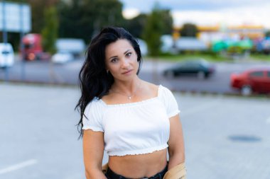 Kırpılmış beyaz bluzlu bir kadın gün batımında dışarıda duruyor. Gün batımında bir kadın kendine güvenerek poz verir..