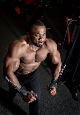 Vücut geliştirici geceleri spor salonunda kablo sineği egzersizi yapıyor. Vücut geliştiren biri, loş bir spor salonunda kablo sineği egzersizi yapar..