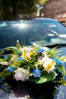 Güneşli bir öğleden sonra araba kaputunda çiçek aranjmanı. Canlı bir buket çiçek, öğleden sonra güneşiyle aydınlatılan bir arabanın kaputunda yatıyor..