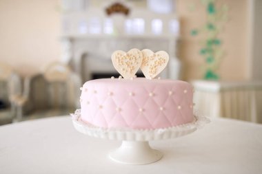 Özel bir etkinlikte kalp kapaklarıyla süslenmiş zarif pembe pasta. Güzel dekore edilmiş pembe bir pasta, beyaz bir stantta kalp şeklinde toplar, kutlama için mükemmel..