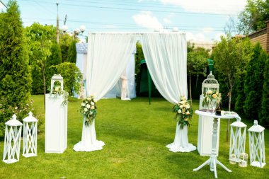 Yeşillik bir bahçede şık bir açık hava düğün töreni. Güzel düzenlenmiş bir düğün sunağı. Kumaşlı kumaş ve çiçek aksanlı bir bahçe..