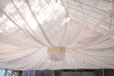 Şık beyaz kumaşlar bir etkinlik mekanında bir tepe örtüsü oluşturuyor. Tavandaki yumuşak beyaz kumaş şelaleleri özel bir olay için romantik bir ortam yaratıyor..