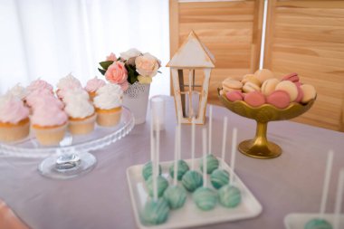 Cupcakeler, badem kurabiyeleri ve şekerlerle dolu canlı bir tatlı masası. Bir tatlı masasında kapkekler, kurabiyeler, pastalar ve şenlikli bir etkinlik için çiçekler var..
