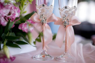 Düğünler için dantelli ve çiçekli şampanya kadehleri. Güzel dekore edilmiş şampanya kadehleri dantel ve fiyonklarla süslenmiş taze çiçeklerin yanında..