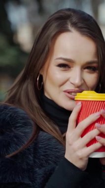 Koyu saçlı, lüks kürk manto giyen, elinde kahve ile kağıt bardak tutan güzel, şehvetli bir kızın moda videosu. Dikey video