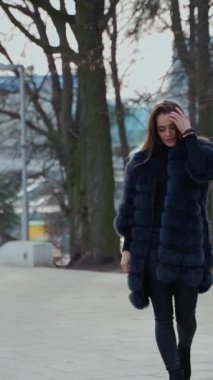 Sonbahar parkında koyu renk saçlı, lüks kürk giyen çekici bir kadının açık hava videosu. Dikey video