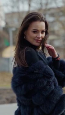 Parkta poz veren şık, koyu renk kürklü bir bayan. Manken yan bakıyor. Kadın moda konsepti. Şehir yaşam tarzı. Moda videosu. Dikey video