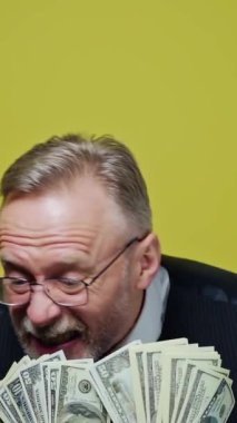 Elinde dolarlarla mutlu yaşlı bir adam. Pozitif zengin adam parasını gösteriyor. Parası olan komik bir kıdemli adamın yüzü. Yakın plan. Dikey video