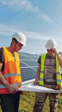 Güneş panellerinin kurulumu. İşçiler yeni güneşli hücrelerin planlarını tartışıyor. Mühendisler güneş çiftliğindeki fotovoltaik panellerden bahsediyorlar. Dikey video