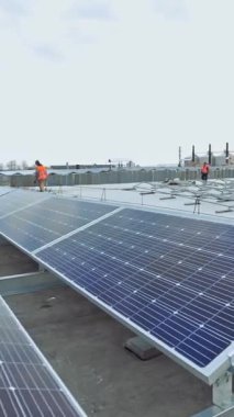 Çatıda bir sürü güneş paneli var. İşçiler güneşli piller kuruyor. Güneş enerjisi üretim fabrikasının dikey video düzenlemesi