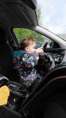 Arabada oynayan küçük sevimli çocuk. Direksiyon şakacı çocuk. Dikey video.