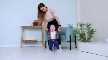 Küçük tatlı çocuk annesiyle yürümeye çalışıyor. İlk adımları atmak için oğlunu tutan kadın..