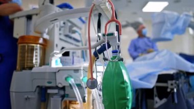 Doktorun aletleri cihazda asılı. Modern akciğer havalandırma makinesinde stetoskop ve ambu torbası var. Cerrah arka planda bulanık çalışıyor.