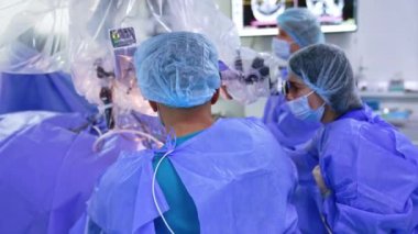 Ameliyathanede çalışan bir grup doktor. Beyin cerrahları mikroskoba dikkatle bakar.