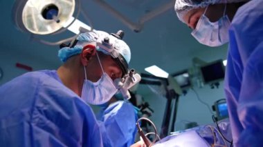 Hastanın üzerinde oturan erkek cerrah elektrikli cerrahi cihazı uyguluyor. Kadın sıhhiyeci doktora yardım ediyor. Düşük açı görünümü.