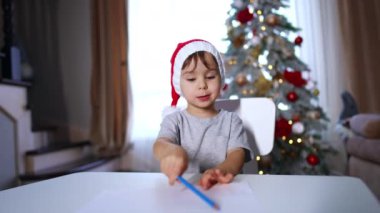 Kırmızı Noel Baba şapkalı, mavi kalemli, beyaz, sevimli bir oğlan. Noel için dekore edilmiş sevimli çocuk..