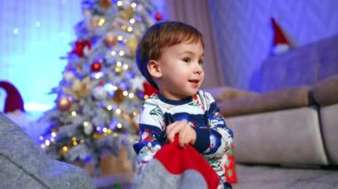 Güzel, gülümseyen bir çocuk elinde çorap, içinden şeker çıkartıyor. Bebek çocuk tatlıları aldığı için mutlu. Arkaplanda Noel ağacı.