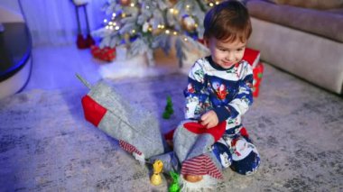 Yerde çoraplarıyla oturan sevimli, beyaz bir bebek var. Mutlu çocuk tatlıları çeker ve kurnazca gülümser..