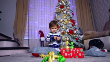 Güzel çocuk yerde oturup hediye kutuları ve şekerlemelerle oynuyor. Çocuklar için mutlu Noeller..