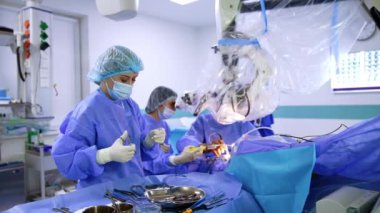 Nöroşirürji cerrahisinde yardımcı hemşire doktor için araç ve malzeme hazırlar. Hastayı ameliyat eden cerrah mikroskoba bakar..