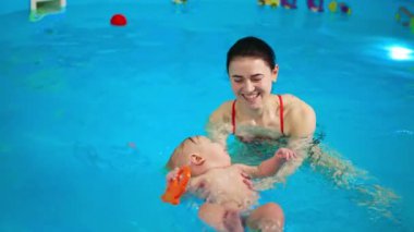 Yüzme havuzunda su yüzeyinde yatan bebeği destekleyen gülümseyen bir kadın. Bayan koç bir çocukla yüzme dersi alıyor..