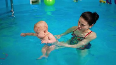 Yüzme havuzunda küçük bir bebeği tutan esmer kadın. Sevimli çocuk neşeyle su sıçratıyor..