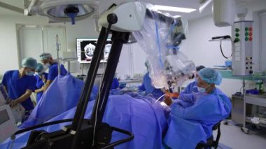 Modern teknolojik mikroskop hastanın üstündeki ameliyathanede duruyor. Operasyon masasında oturan beyin cerrahı, dürbünün uygulanmasına bakıyor..