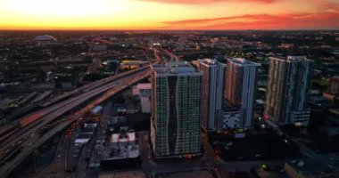 Gün batımında metropolde bir sürü araba gidip geliyor. Arka planda turuncu gökyüzü olan Miami manzarası. Üst görünüm.