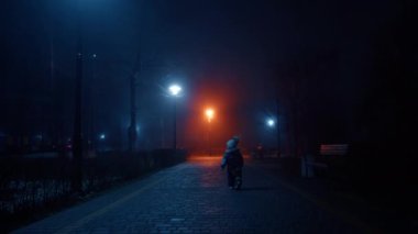 Sıcak giysili küçük bebek kameradan kaçıyor. Gece vakti kış parkında yürüyen bir çocuk..