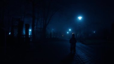 Sıcak kıyafetler giyen küçük bir çocuk gece karanlık sokakta yürüyor. Elinde kitap tutan bebek kameraya bakmayı keser..