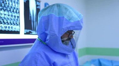 Koruyucu giysi ve kask giyen erkek cerrah. MRI taramalarıyla ekranda duran bir doktorun yan görünüm portresi.