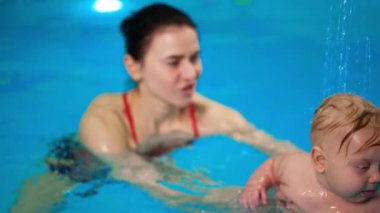 Esmer kadın bebeği yüzme havuzunda akan suyun altına koydu. Bebeğe yüzmeyi öğretiyorum..
